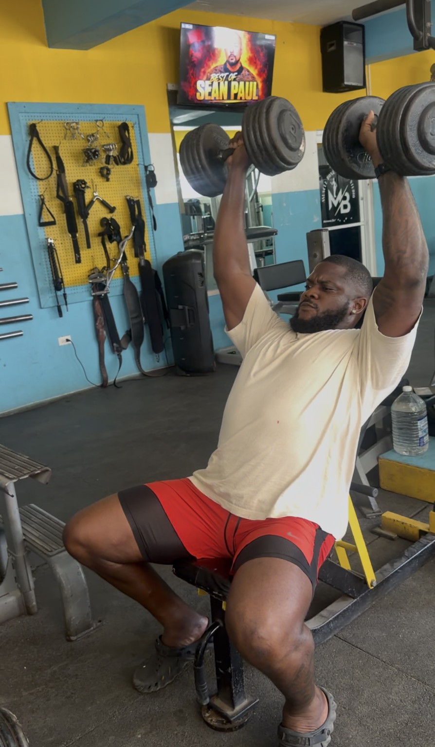 Coach Muscle performing a seated dumbbell shoulder press at Muscle Bones Fitness Studio